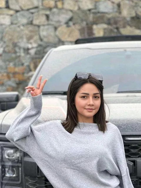 Woman in a grey sweater waving outdoors